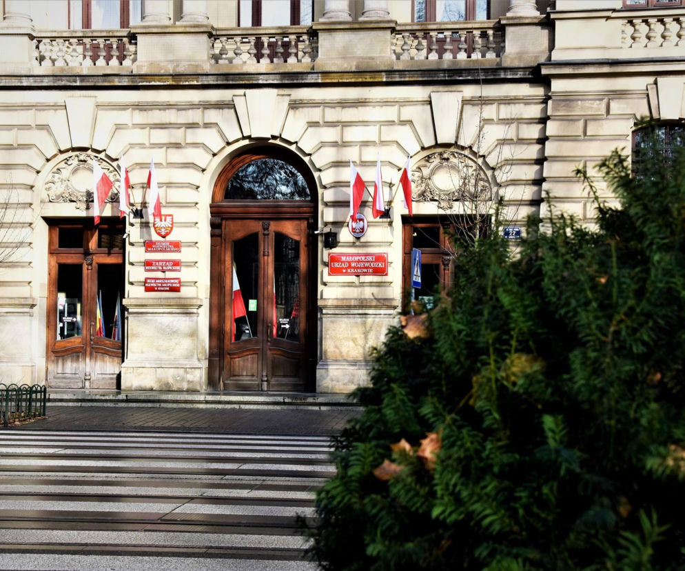 Wejście do Małopolskiego Urzędu Wojewódzkiego w Krakowie z flagami Polski. O nowej inwestycji MUW przeczytasz na Muratorplus.