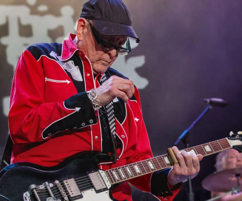 Rick Nielsen z Cheap Trick w czerwonej koszuli gra na gitarze. O aukcji jego kolekcji instrumentów przeczytasz na EskaRock.