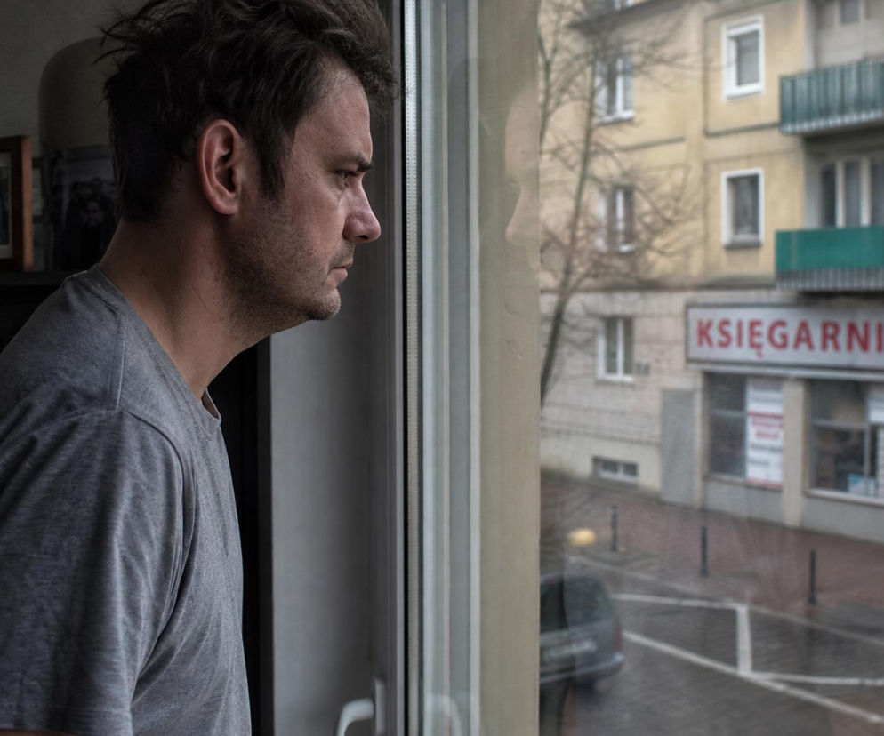 Zasmucony mężczyzna patrzy przez okno na budynek z napisem księgarnia. O trudnych relacjach przeczytasz na SE.