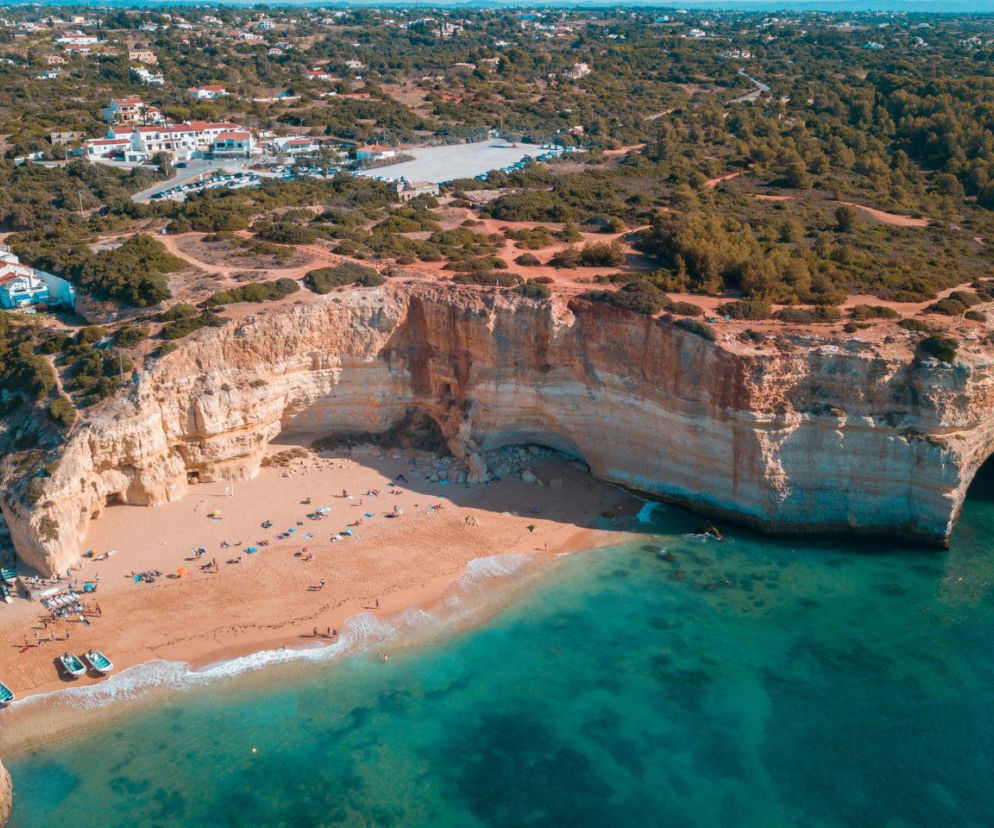 Plaża w regionie Algarve z jasnym piaskiem i wysokimi klifami nad błękitną wodą. O urlopie w Portugalii przeczytasz w Eska.