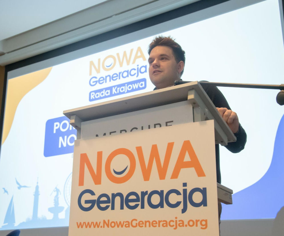 Mężczyzna w czarnej koszuli przemawia z mównicy z napisem NOWA Generacja Rada Krajowa i logo Nowej Generacji, z banerem NOWA Generacja Rada Krajowa w tle. To Dawid Kacprzyk, oświadczający się w sprawie zarzutów, o czym więcej przeczytasz na naszym portalu.
