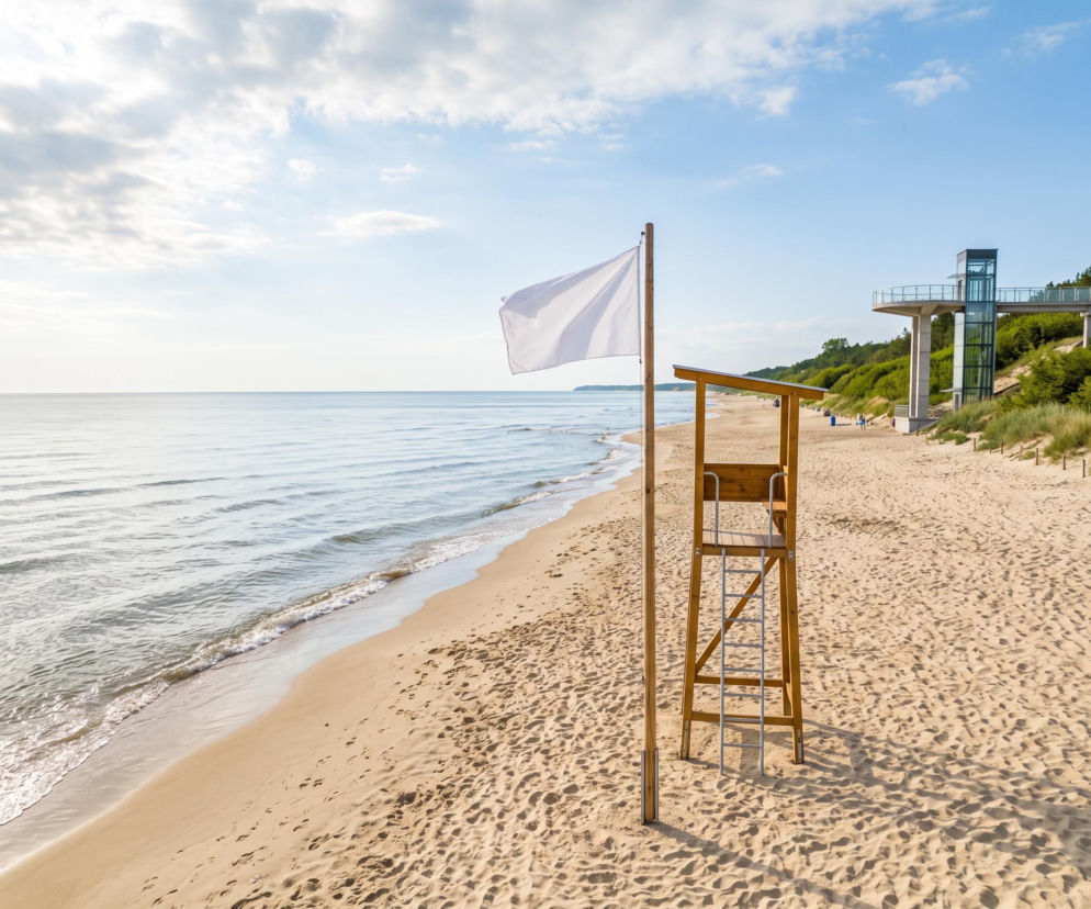 Biała flaga na plaży w Pobierowie obok wieży ratowniczej i tarasu widokowego. O pogodzie przeczytasz na SE Szczecin.