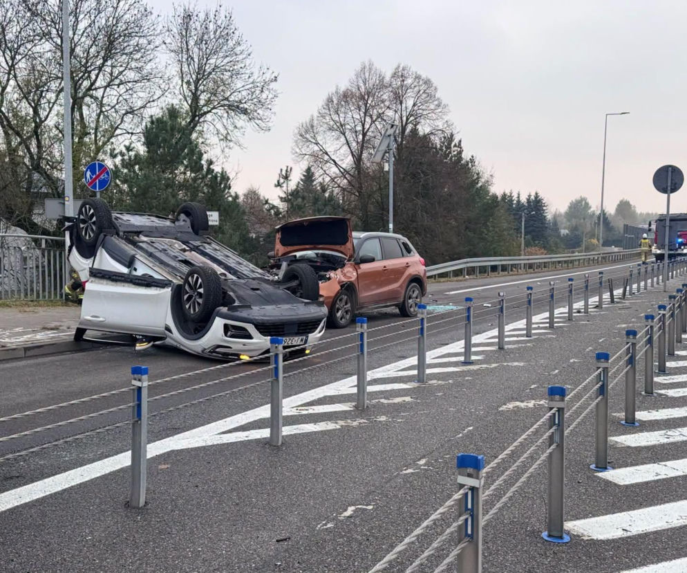 Białe auto leżące na dachu po wypadku na DK94. Obok uszkodzone suzuki i straż pożarna. O zdarzeniu czytaj w Eska Tarnów.