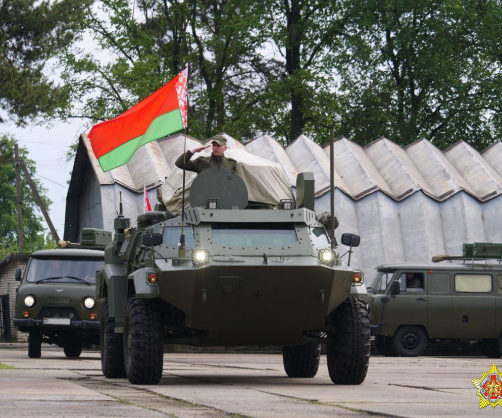 Żołnierz salutujący z transportera opancerzonego z flagą Białorusi. O manewrach przy granicy przeczytasz w Eska.