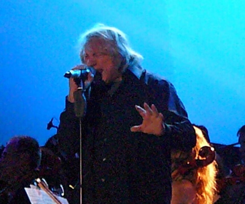 Wokalista Lou Gramm śpiewa do mikrofonu na scenie. O pożegnaniu artysty z estradą przeczytasz na EskaRock.