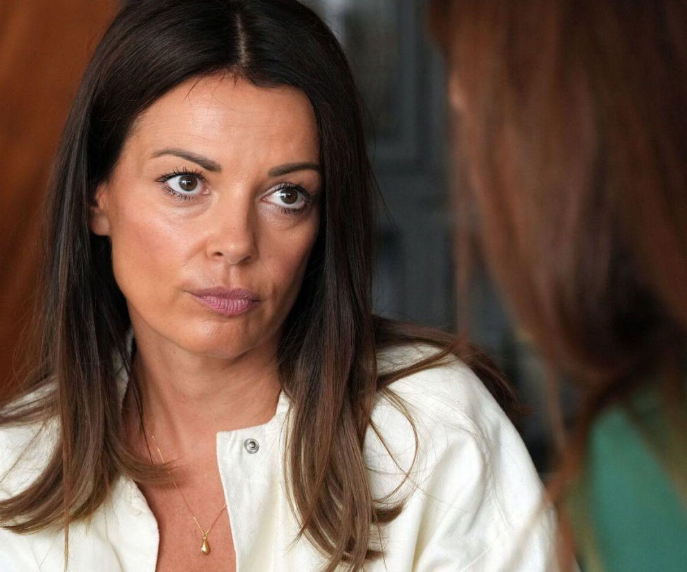 Zaniepokojona Kasia, postać z Barw szczęścia, rozmawia z Celiną, intensywnie wpatrując się w nią. W tle widać brązowe, rozmyte tło. Kasia ma na sobie białą koszulę i złoty naszyjnik. Więcej o losach bohaterów na portalu Super Seriale.