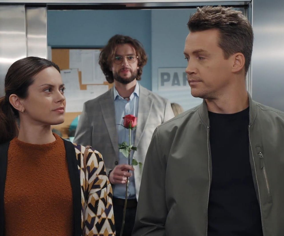 Paulina Lasota (Kasia) i Krzysztof Kwiatkowski (Jakub) patrzą na siebie w windzie, za nimi Mateusz Mosiewicz (Mariusz) z różą, sugerując napięcie emocjonalne przed oświadczynami. Więcej o losach bohaterów przeczytasz na portalu Super Seriale.