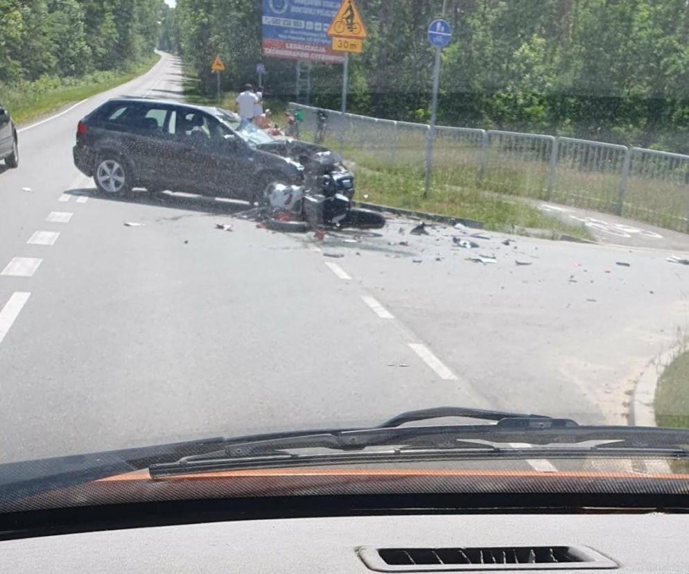 Samochód osobowy z mocno uszkodzonym przodem po zderzeniu z motocyklem w Olszewicach, elementy rozbitego pojazdu leżą na jezdni. W tle widać drogę i drzewa. Więcej informacji o wypadkach drogowych przeczytasz na naszym portalu.