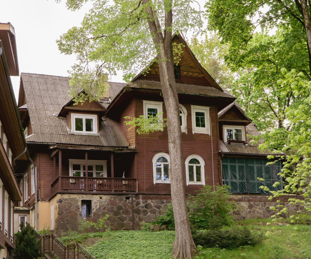 Drewniana willa w stylu zakopiańskim, z charakterystycznym półszczytowym dachem i werandą, stojąca wśród zieleni na wzniesieniu przy ulicy Paca w Wilnie. O jej niezwykłej historii można przeczytać na Architektura Murator Plus.