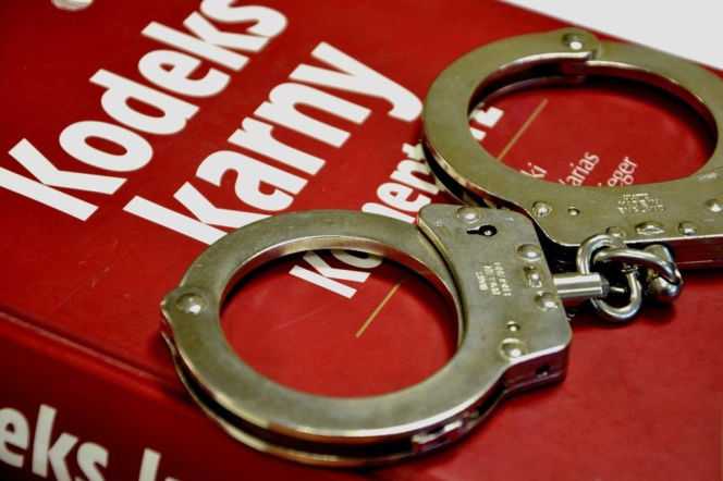 Srebrne kajdanki leżące na czerwonej okładce Kodeksu Karnego. O karze za rozbój przeczytasz na Eska Nowy-Sącz.