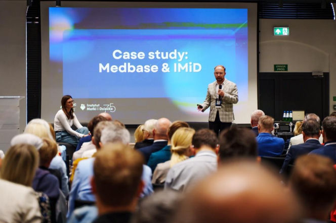 Mężczyzna przemawiający na tle ekranu z napisem Case study: Medbase i IMiD. O wynikach pilotażu czytaj w Poradnik Zdrowie.