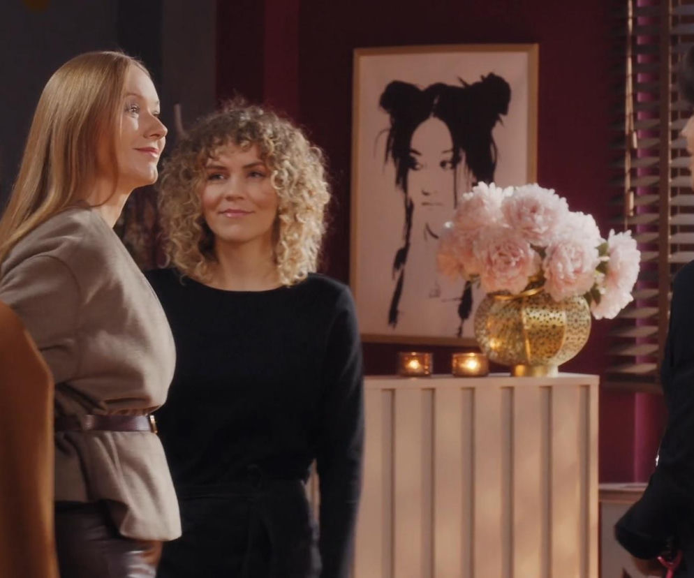 Kobiety w salonie fryzjerskim: Elżbieta w beżowej bluzce z paskiem oraz Kama z kręconymi włosami w czarnej bluzce patrzą na trzecią kobietę z boku. Scena z serialu M jak miłość przedstawia ostrą konfrontację Kamy i Elżbiety, której szczegóły poznasz na Super Seriale.