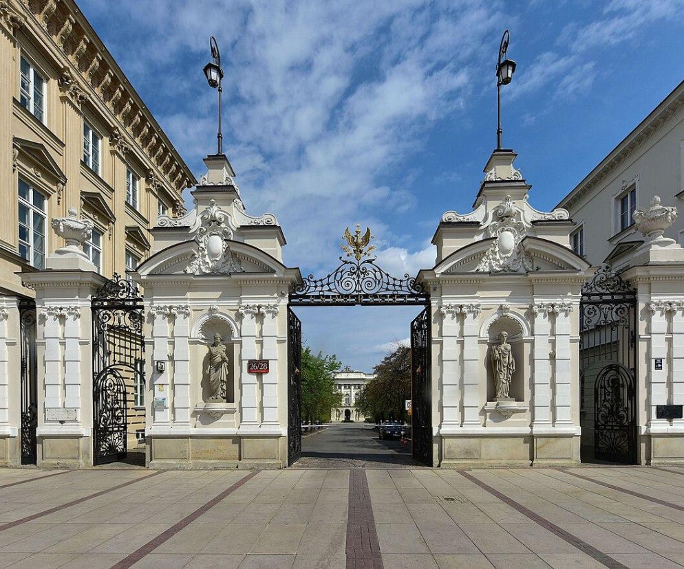 Brama główna Uniwersytetu Warszawskiego, zdobiona rzeźbami i kutymi elementami, otwarta na teren uczelni, symbolizuje zagrożenie WZW A. Na Poradniku Zdrowie dowiesz się o objawach, profilaktyce i postępowaniu w przypadku zakażenia wirusem na UW.