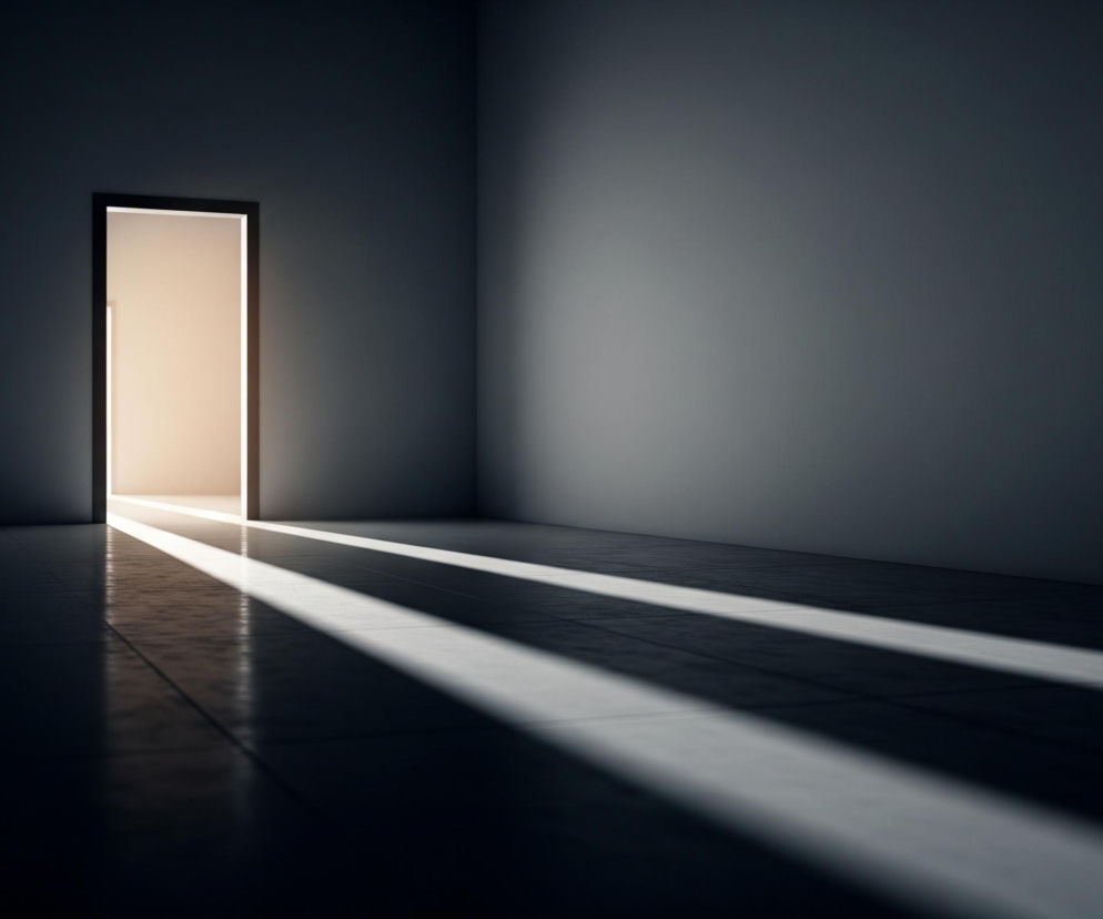 Po lewej stronie obrazu znajduje się otwarte przejście lub drzwi, z wnętrza którego wydobywa się jasne, ciepłe światło o beżowo-pomarańczowym zabarwieniu. Światło to rzuca długie, równoległe pasma na ciemną podłogę w pomieszczeniu, oświetlając trzy wyraźne smugi na ciemnym, płytkowym podłożu, tworząc kontrast z resztą cienia. Ściany i sufit pokoju są utrzymane w ciemnych odcieniach szarości, niemal granatu, z delikatnymi przejściami tonalnymi, sugerującymi subtelne oświetlenie górne lub boczne, które podkreśla minimalistyczny charakter wnętrza.