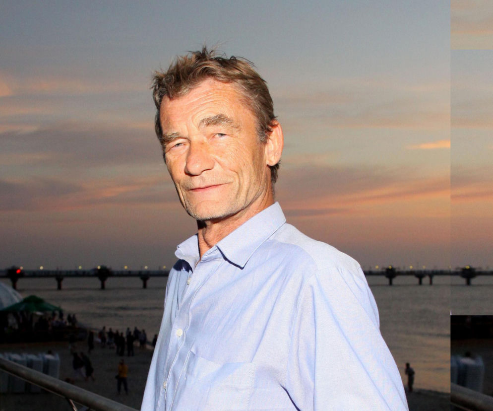 Aktor Krzysztof Kiersznowski w niebieskiej koszuli na tle molo i zachodu słońca. O jego karierze przeczytasz na SE.
