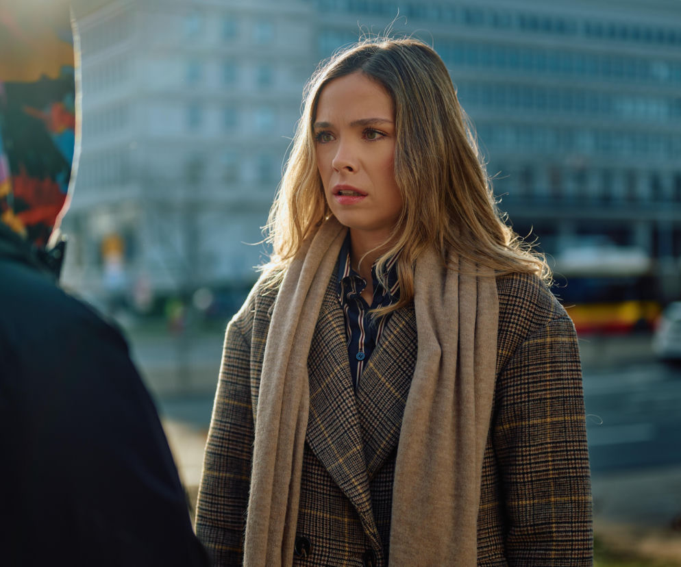 Wzburzona Kalina w beżowym szaliku i płaszczu w kratę, skonfliktowana z Łukaszem, podczas publicznej sceny. Emocje sięgają zenitu w odcinku 4161 serialu Na Wspólnej, o czym przeczytasz więcej na portalu Super Seriale.