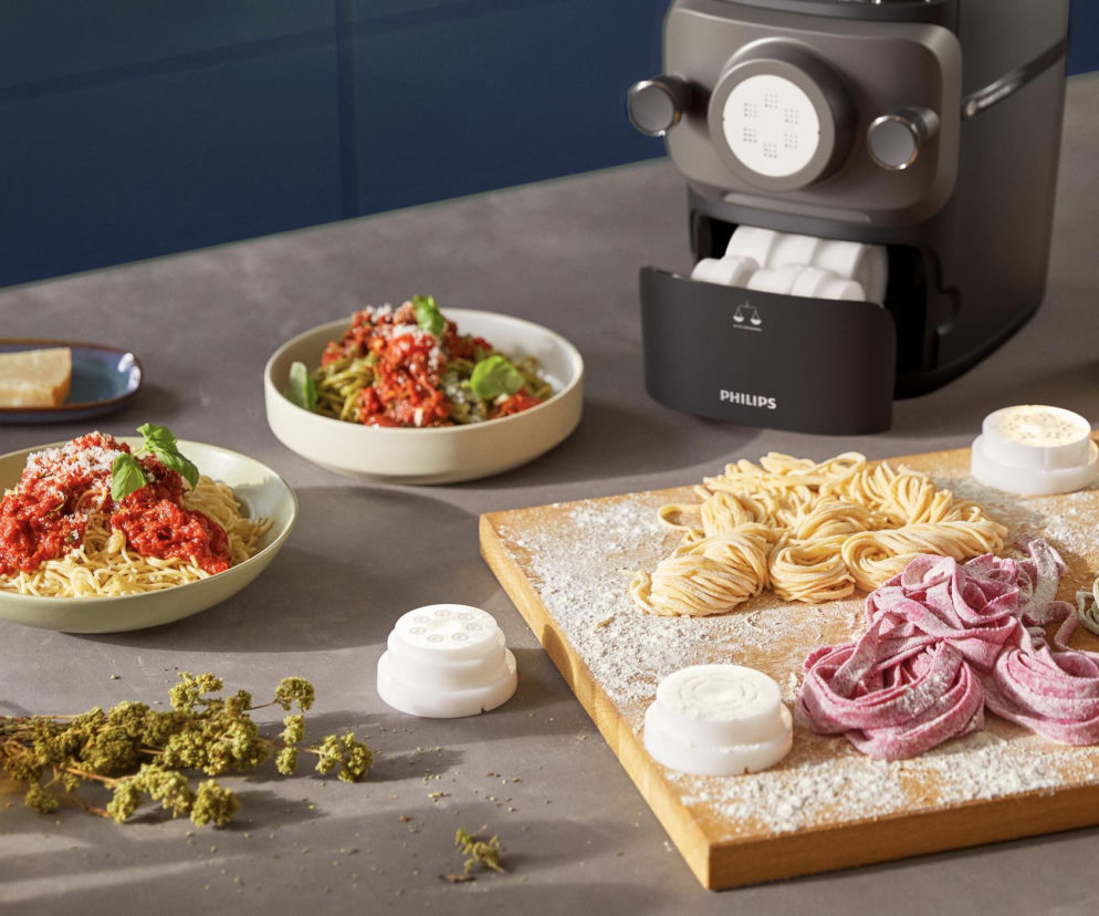 Philips Pasta Maker obok talerzy z daniami i kolorowego makaronu. O domowych smakach przeczytasz na Eska2.