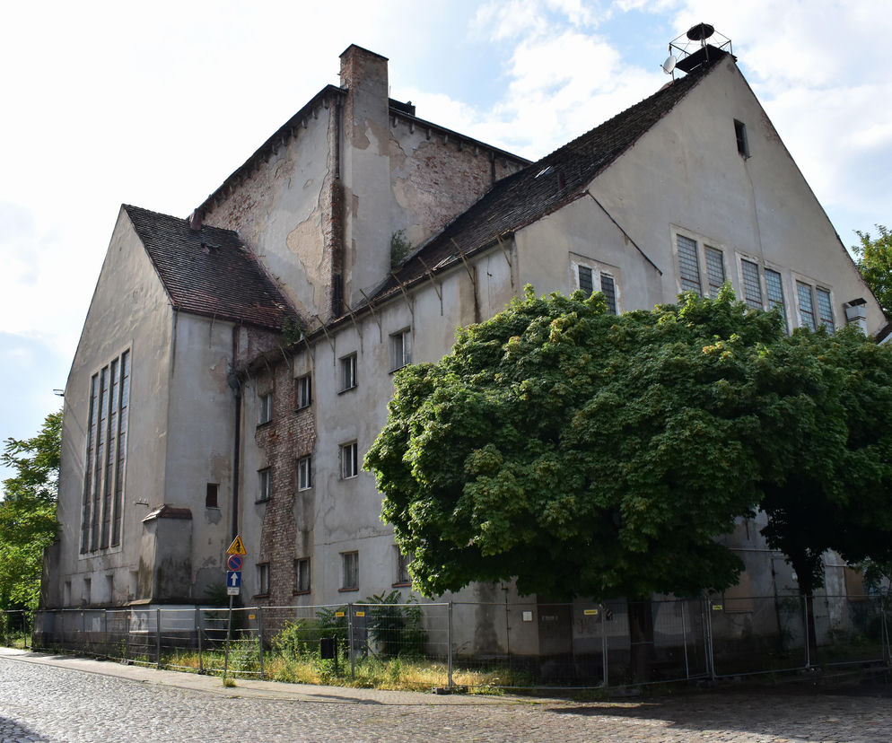 Nowa Synagoga w Poznaniu, zniszczona elewacja i ceglane ściany, otoczona metalowym ogrodzeniem. Obiekt, dawniej pływalnia, a obecnie wystawiony na sprzedaż, ma skomplikowaną historię. Więcej o architekturze tego zabytku przeczytasz na Architektura Murator Plus.