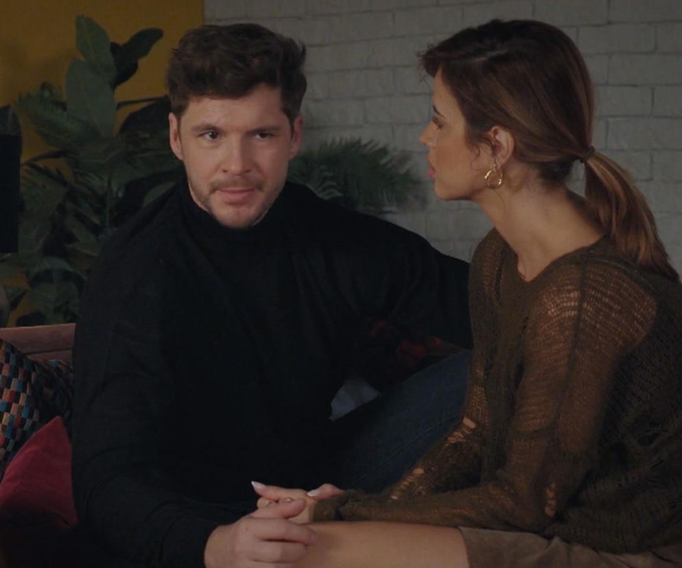 Marcin (Mikołaj Roznerski) i Kama (Michalina Sosna) z serialu M jak miłość siedzą obok siebie, on spogląda w obiektyw, ona odwrócona. Marcin ma na sobie czarny golf, Kama brązowy sweter. Zdjęcie ilustruje sceny z odcinka 1932, gdzie Marcin oszuka Kamę w sprawie szefowej. Więcej na Super Seriale.