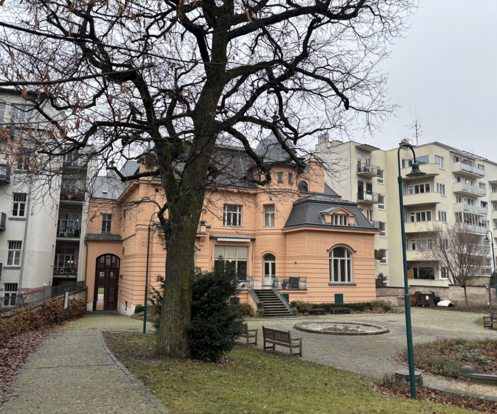 Secesyjna Willa Löw-Beer w Brnie z jasnopomarańczową elewacją i szarym dachem, widoczna w zimowym otoczeniu, z bezlistnym drzewem na pierwszym planie oraz nowoczesnymi budynkami w tle. O jej historii i architekturze przeczytasz na Architektura Murator Plus.