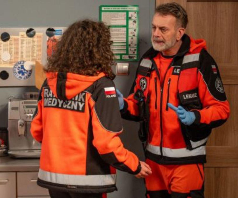 Dwie osoby w strojach ratowników medycznych. Jedna z nich odwrócona tyłem, z napisem RATOWNIK MEDYCZNY i flagą Polski. Druga osoba, starszy mężczyzna z brodą, odziana w kurtkę z napisem LEKARZ, mówi coś do niej. Omawiają wydarzenia z 888 odcinka Na sygnale, o których przeczytasz na Super Seriale.