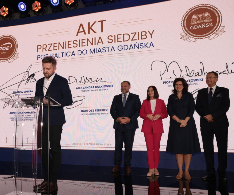 Osoby na tle ekranu z napisem Akt przeniesienia siedziby PGE Baltica do Gdańska. O zmianach w Grupie PGE przeczytasz na SE.