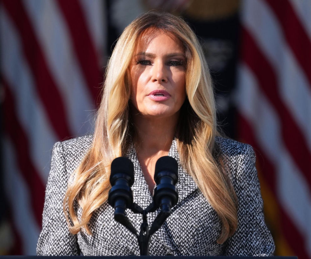 Melania Trump przemawiająca przy mikrofonach na tle flag USA. O jej roli w zawieszeniu broni przeczytasz na SE.