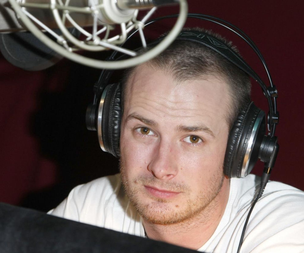 Aktor Paweł Małaszyński w słuchawkach przy mikrofonie w studio. O jego hołdzie dla lidera Queen przeczytasz na EskaRock.