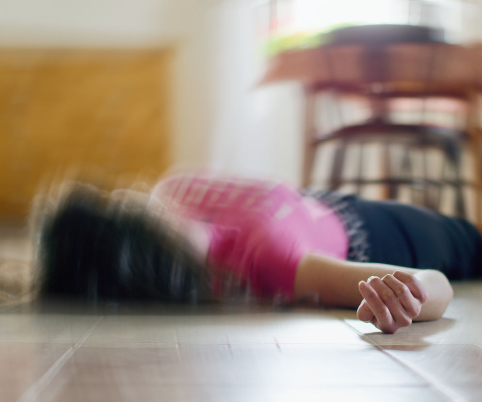 Osoba leżąca na podłodze z rozmazanym ruchem, symbolizująca atak padaczki. Zdjęcie ilustruje trudności i wyzwania związane z chorobą, a także podkreśla potrzebę wiedzy, jak reagować w takich sytuacjach. Więcej o padaczce przeczytasz na Poradnik Zdrowie.