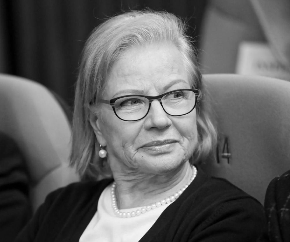 Czarno-białe zdjęcie Bożeny Dykiel, aktorki z siwymi włosami, w okularach, perłowym naszyjniku i kolczykach, w czarnym kardiganie i białej bluzce. Uśmiecha się, patrząc w prawo. Aktorka mierzyła się z chorobami serca i depresją, o czym można przeczytać na portalu Poradnik Zdrowie.