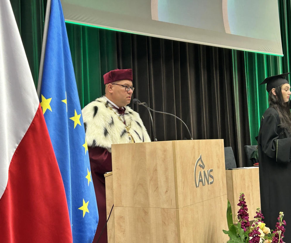 Rektor Akademii Nauk Stosowanych w Koninie, Artur Zimny, w todze rektorskiej przemawia z mównicy z logo uczelni. Obok niego polska i europejska flaga. Studenci mogą poznać szczegóły rekrutacji na naszej stronie naszym portalu.