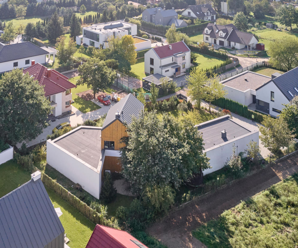 Współczesne domy jednorodzinne, widoczne z lotu ptaka, prezentują różnorodne elewacje i dachy, z przewagą zielonych ogrodów i naturalnego zacienienia, co pomaga w ochronie przed upałami. Więcej o projektowaniu domów odpornych na wysokie temperatury przeczytasz na Architektura Murator Plus.