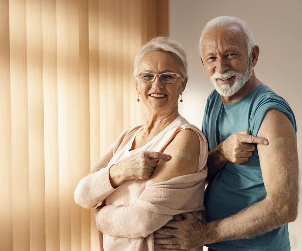 Uśmiechnięta starsza para w średnim zbliżeniu, kobieta i mężczyzna, pokazujący plastry po szczepieniu na ramionach. Promują profilaktykę HPV u seniorów, o której można przeczytać na portalu Poradnik Zdrowie.