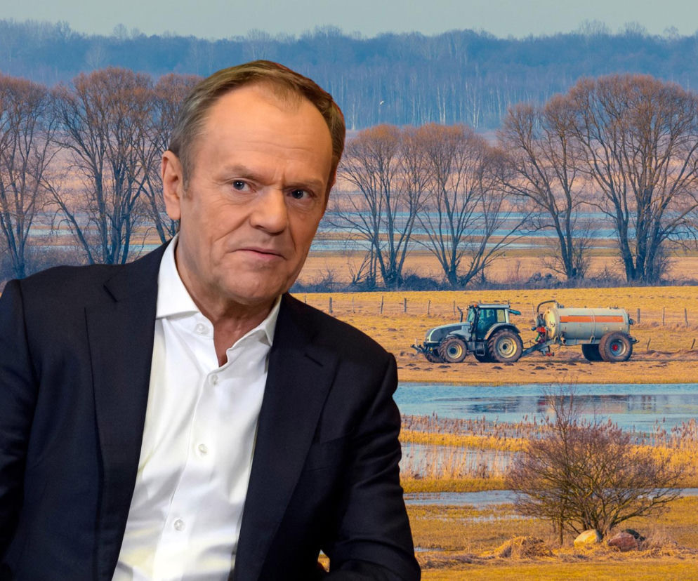 Donald Tusk na tle pola i lasu z traktorem, symbolizującym kwestie gruntów rolnych i rolnictwa. Tusk, w białej koszuli i marynarce, patrzy wprost, jego wizerunek łączy się z tematami polityki rolnej, o której można przeczytać na Super Biznes.