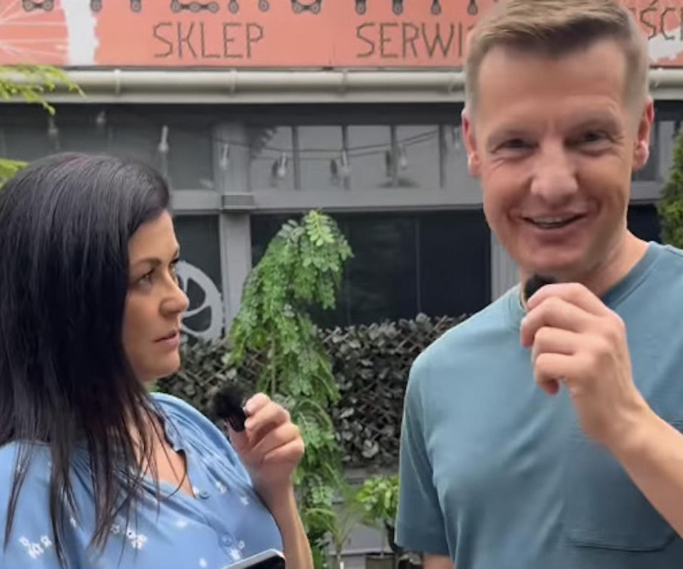 Katarzyna Cichopek i Rafał Mroczek w kadrze z nagrania, ubrani w casualowe stroje, przybliżają fanom M jak miłość kulisy historii Bistro Kingi. Na tle budynku z napisem Sklep Serwis aktorzy z uśmiechem prezentują szczegóły z przeszłości serialowych bohaterów. Więcej o Super Seriale przeczytasz na naszym portalu.