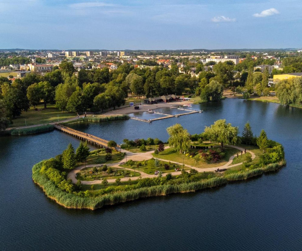 Widok z góry na Zalew Arkadia w Suwałkach z zieloną wyspą i kładką. O urokach Suwalszczyzny przeczytasz na SE.