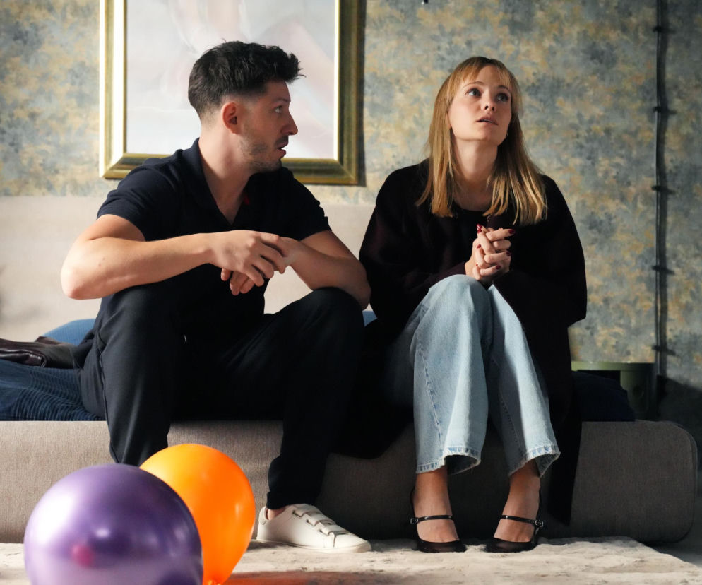 Justin (Jasper Sołtysiewicz) i Ola (Michalina Robakiewicz) siedzący na łóżku, otoczeni balonami. Justin w czarnej koszulce i spodniach, Ola w jeansach i ciemnej bluzce, z zaniepokojoną miną. Zdjęcie ilustruje fragment artykułu o serialu Barwy Szczęścia na Super Seriale.