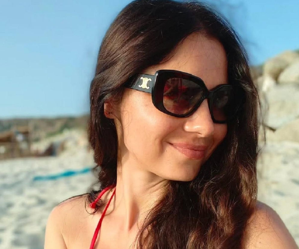 Uśmiechnięta Adriana Kalska w okularach przeciwsłonecznych na plaży. O urlopie aktorki przeczytasz w Eska.