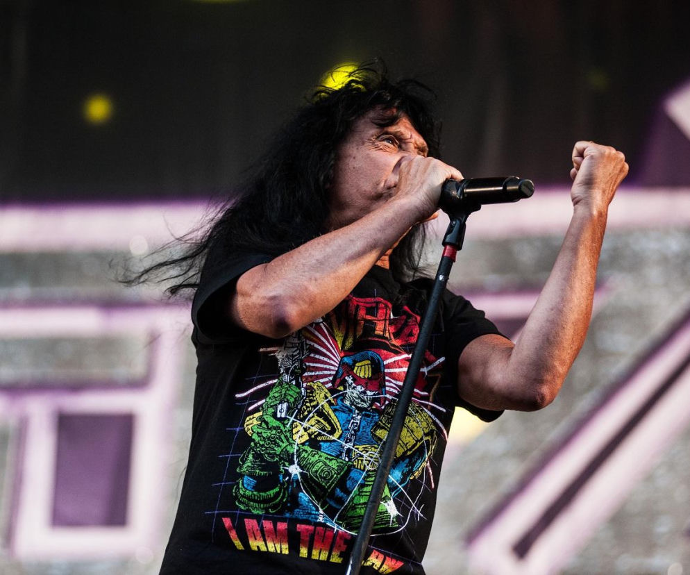 Wokalista Anthrax Joey Belladonna śpiewa do mikrofonu i zaciska pięść. O historii zespołu przeczytasz na EskaRock.