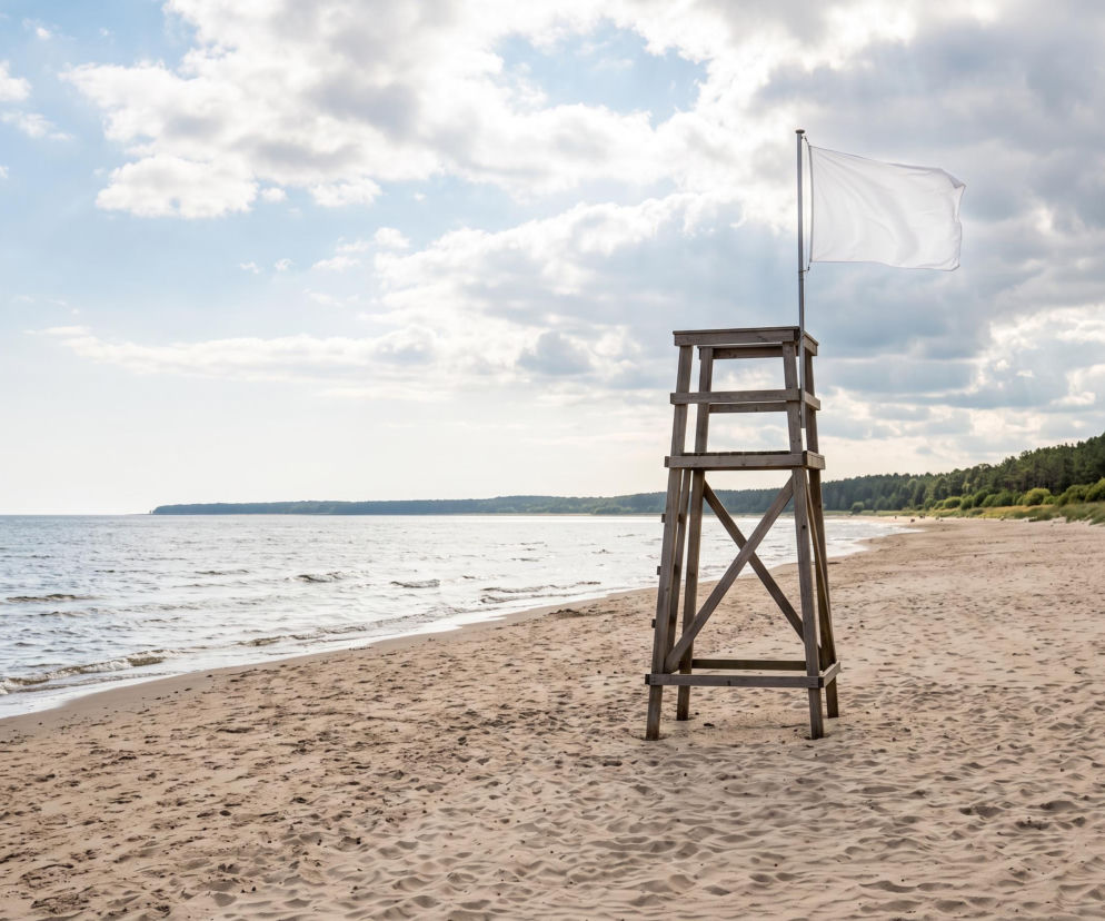 Drewniana wieża ratownika z białą flagą na pustej plaży. O bezpiecznych kąpielach w Dziwnowie przeczytasz na SE Szczecin.