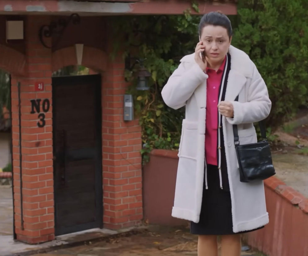 Kobieta w białym płaszczu i różowej koszuli, Cavidan z serialu „Miłość i nadzieja”, rozmawia przez telefon, stojąc przed domem. Jej wyraz twarzy sugeruje zmartwienie lub pilną sytuację. Scena odzwierciedla moment z 352 odcinka, gdy Cavidan próbuje ostrzec Bahar przed pułapką, co można przeczytać na Super Seriale.