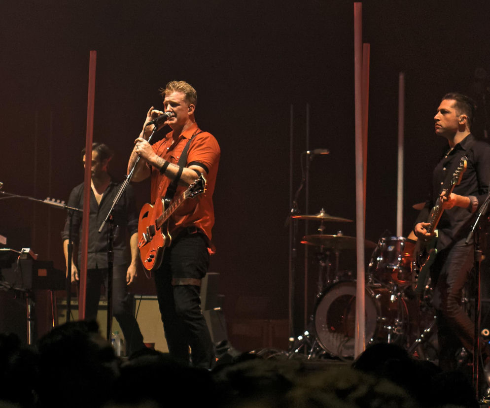 Josh Homme śpiewa i gra na gitarze podczas koncertu Queens of the Stone Age. O ich muzyce przeczytasz w EskaRock.