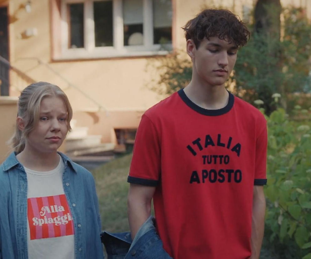 Lenka i Grzesiek w emocjonalnej scenie pożegnania, patrzą w dół ze smutkiem. Lenka ma blond włosy i dżinsową koszulę, Grzesiek koszulkę Italia Tutto a Posto. Koniec ich związku w 1898 odcinku M jak miłość. Więcej informacji o serialu znajdziesz na Super Seriale.