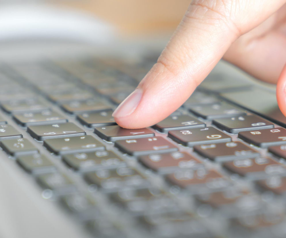 Palec osoby naciskającej klawisz na klawiaturze laptopa. O problemach z e-Doręczeniami przeczytasz na SE Superbiz.