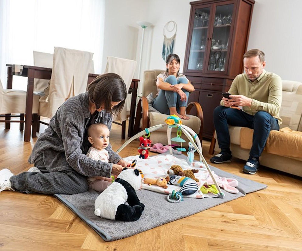 Kobieta, Kinga (Aleksandra Zienkiewicz) w domowych ubraniach bawi się z niemowlęciem na macie edukacyjnej z pluszową pandą. W tle inna kobieta, Lilka (Sylwia Sokołowska) i mężczyzna, Janek (Maciej Mikołajczyk), siedzą, patrząc w telefon. Emocje po poronieniu Kingi będą głównym motorem jej działań, co można przeczytać na Super Seriale.