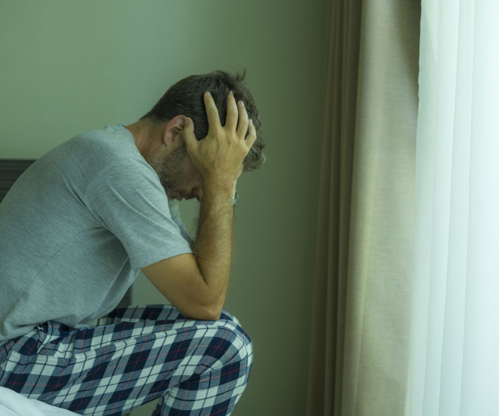 Mężczyzna na łóżku z dłońmi w rękach