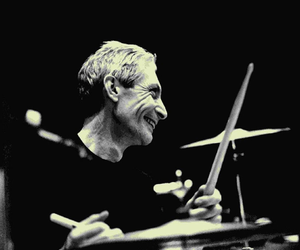 Uśmiechnięty perkusista Charlie Watts gra na bębnach. O historii muzyka The Rolling Stones przeczytasz na EskaRock.