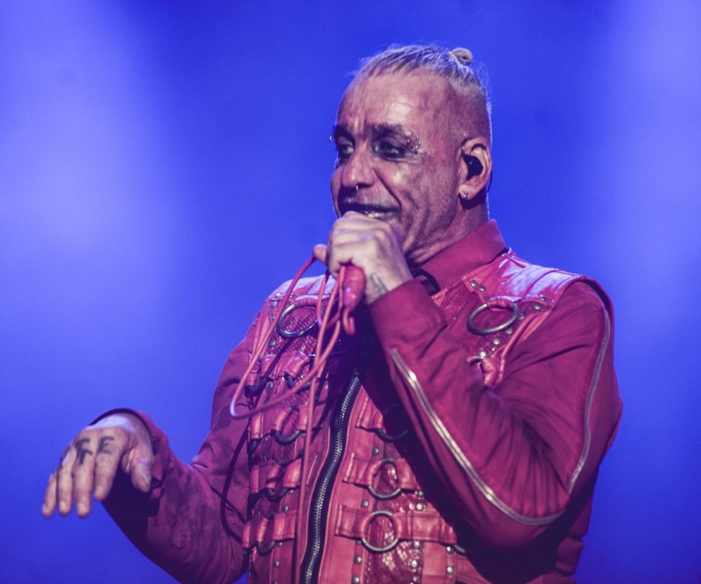 Till Lindemann w czerwonym skórzanym kostiumie śpiewa do mikrofonu. O koncertach artysty przeczytasz na EskaRock.
