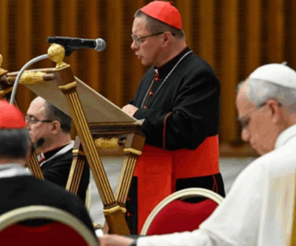 Kardynał Grzegorz Ryś w czerwonym birecie i czarnych szatach liturgicznych, stojący przy pulpicie z mikrofonem, wygłasza medytację biblijną w Watykanie. W tle siedzą inni duchowni, w tym papież Franciszek w białej sutannie. O przemówieniu kardynała przeczytasz na naszym portalu.