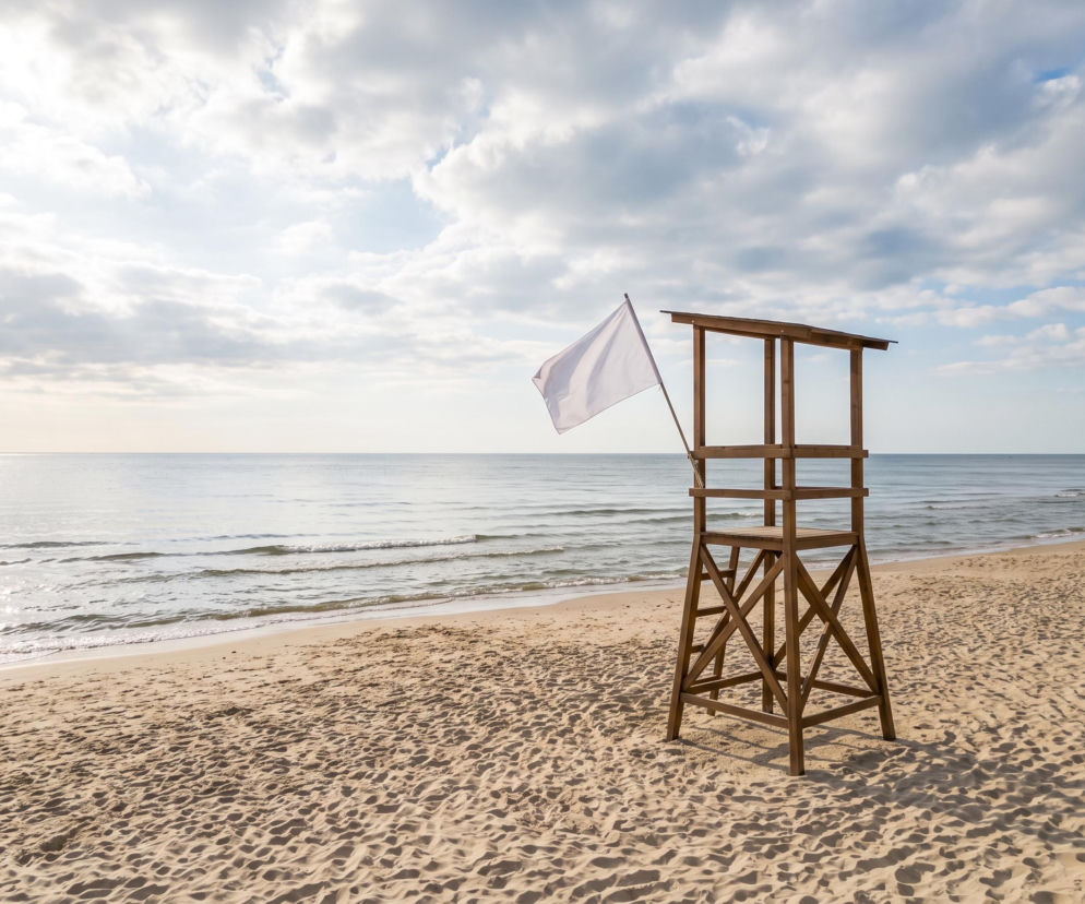 Drewniana wieża ratownicza z białą flagą na pustej plaży. O bezpiecznej kąpieli w Świnoujściu przeczytasz na SE Szczecin.